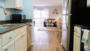 A kitchen with white cabinets, a black refrigerator, and a microwave. There is a dining area with a table and chairs in the background. - Cliffside Cottage 4 - Near SDC, Lake, & Downtown! (Branson)
