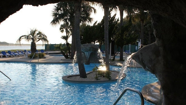 A swimming pool with water features, lounge chairs, palm trees, and a view of the water. - 338 Capt John Fripp Villa W/Cart, Cards Available! (Fripp Island)