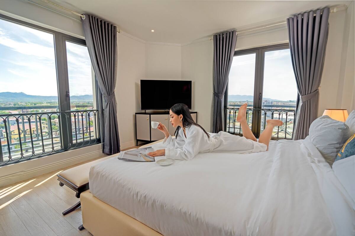 Een hotelkamer met een groot bed, een flatscreen televisie en een balkon met uitzicht op de stad.