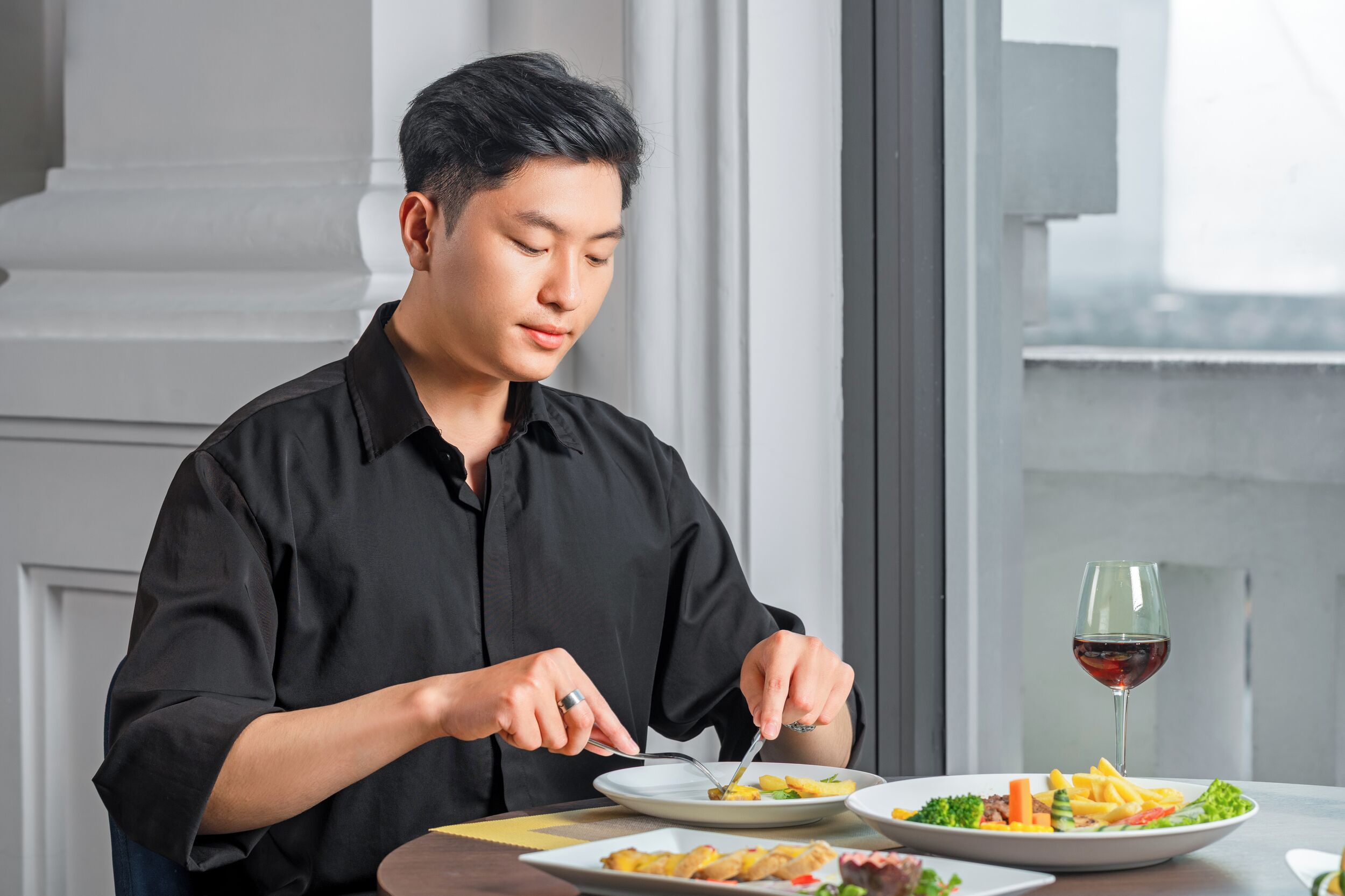 A person dining at a table with a plate of food and a glass of red wine.