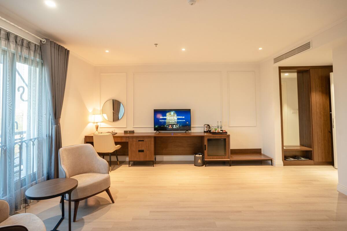 Een moderne hotelkamer met een houten bureau, een televisie, een stoel en een klein tafeltje.