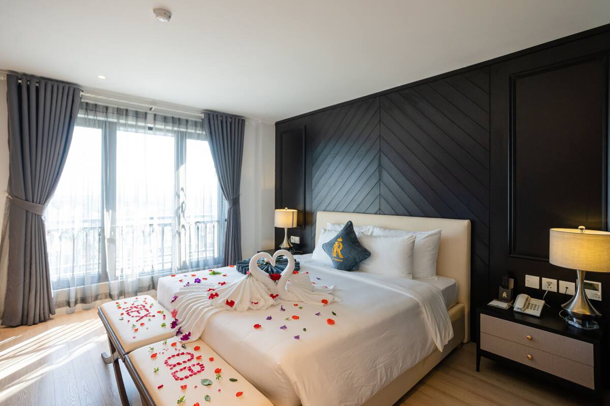 Een hotelkamer met een groot bed, een nachtkastje met een lamp, en een uitzicht op het landschap door het raam.