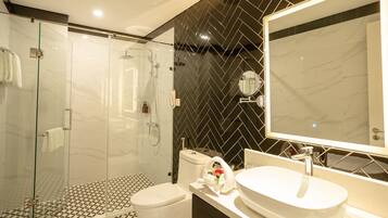 A modern bathroom with a glass-enclosed shower, a white sink, and a black herringbone-patterned wall.