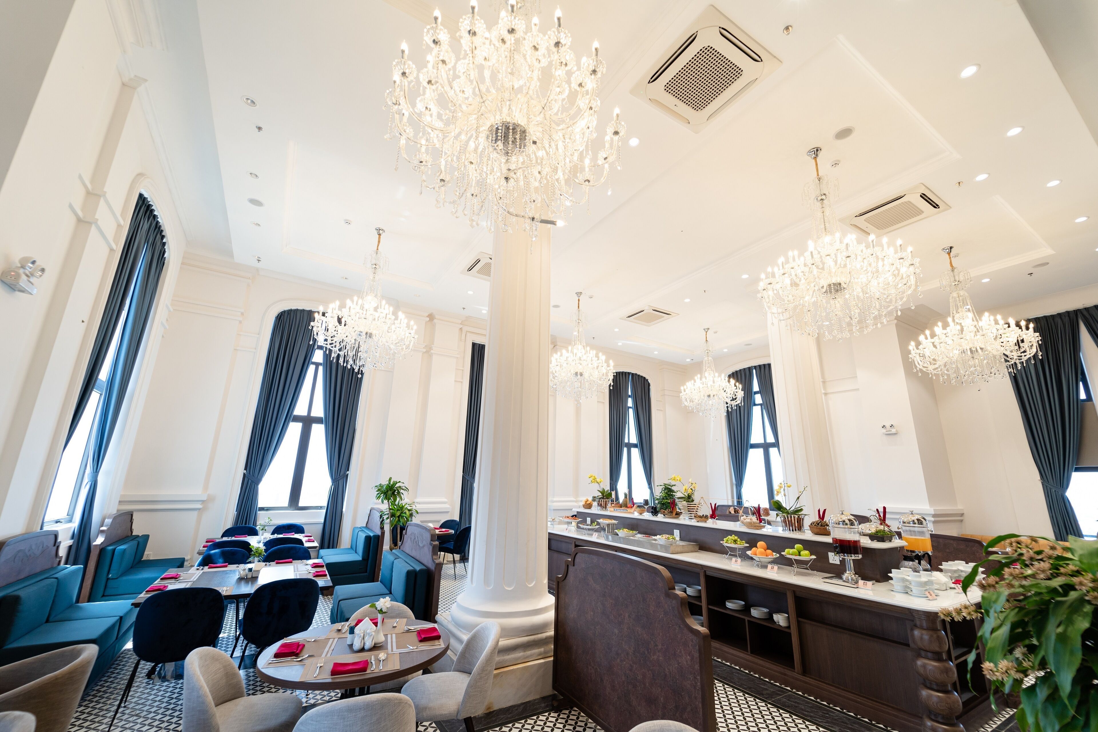Spaziosa sala da pranzo di un hotel, con soffitti alti, grandi lampadari e un bar centrale che offre diverse scelte di cibo e bevande.