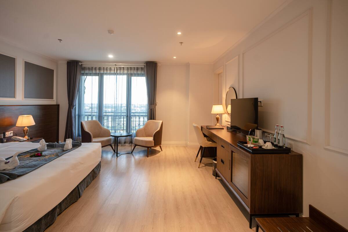 Hotelkamer met een bed, twee stoelen, een bureau, een televisie en een raam met gordijnen.