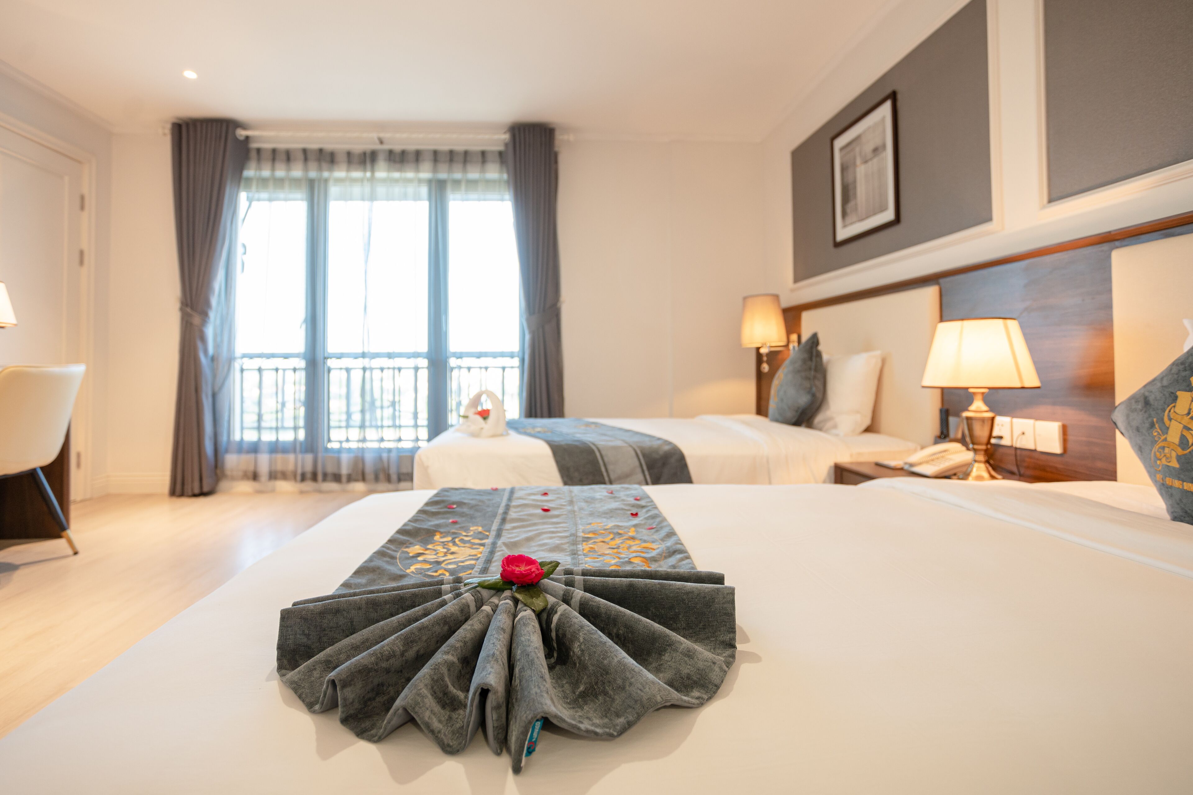 Een hotelkamer met een netjes opgemaakt bed, een zithoek met een fauteuil, een nachtkastje met een lamp, en een groot raam met gordijnen.