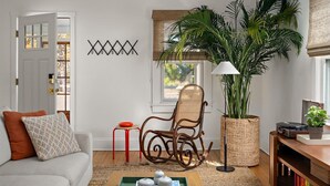 Una sala de estar con un sofá, un sillón mecedora, una mesita auxiliar, una planta en maceta, una lámpara y una estantería.