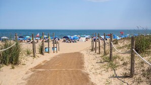 Un sendero arenoso que lleva a una playa con sombrillas y gente.