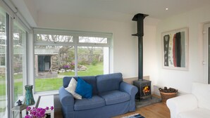 A living room with a blue sofa, a white armchair, a fireplace, and a large window overlooking a garden. - Beautiful views to Inisbofin (Cleggan)