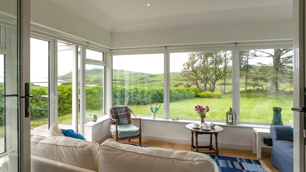A bright room with large windows, a sofa, a chair, and a small table with cups and a vase of flowers. - Beautiful views to Inisbofin (Cleggan)