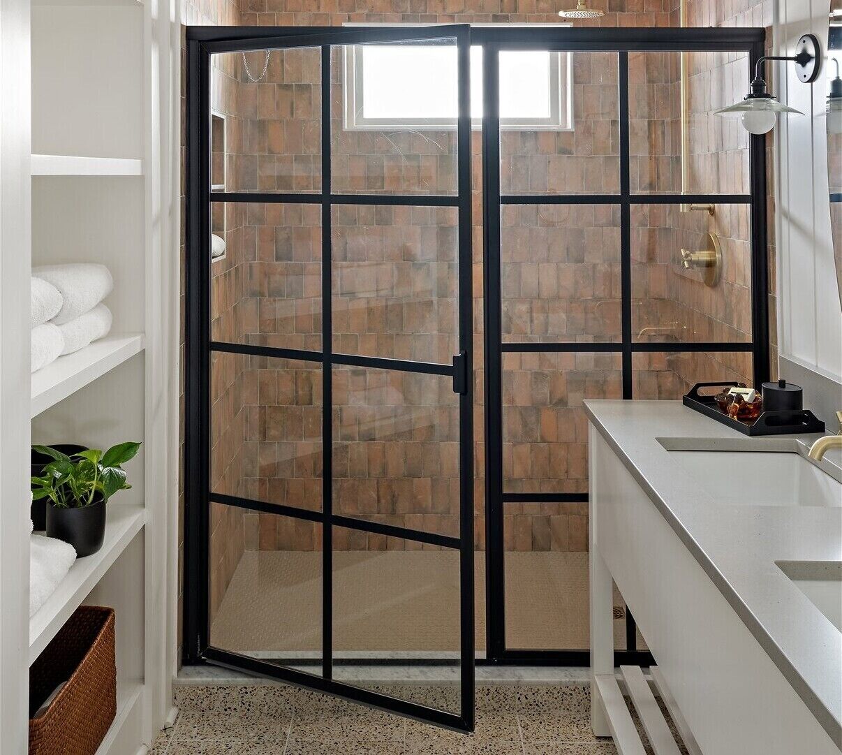 Un baño con puerta de vidrio, estantes blancos, un lavabo y una planta en maceta.