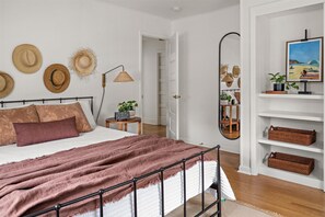 Quarto com cama, mesas de cabeceira, espelho e prateleira com cestos.