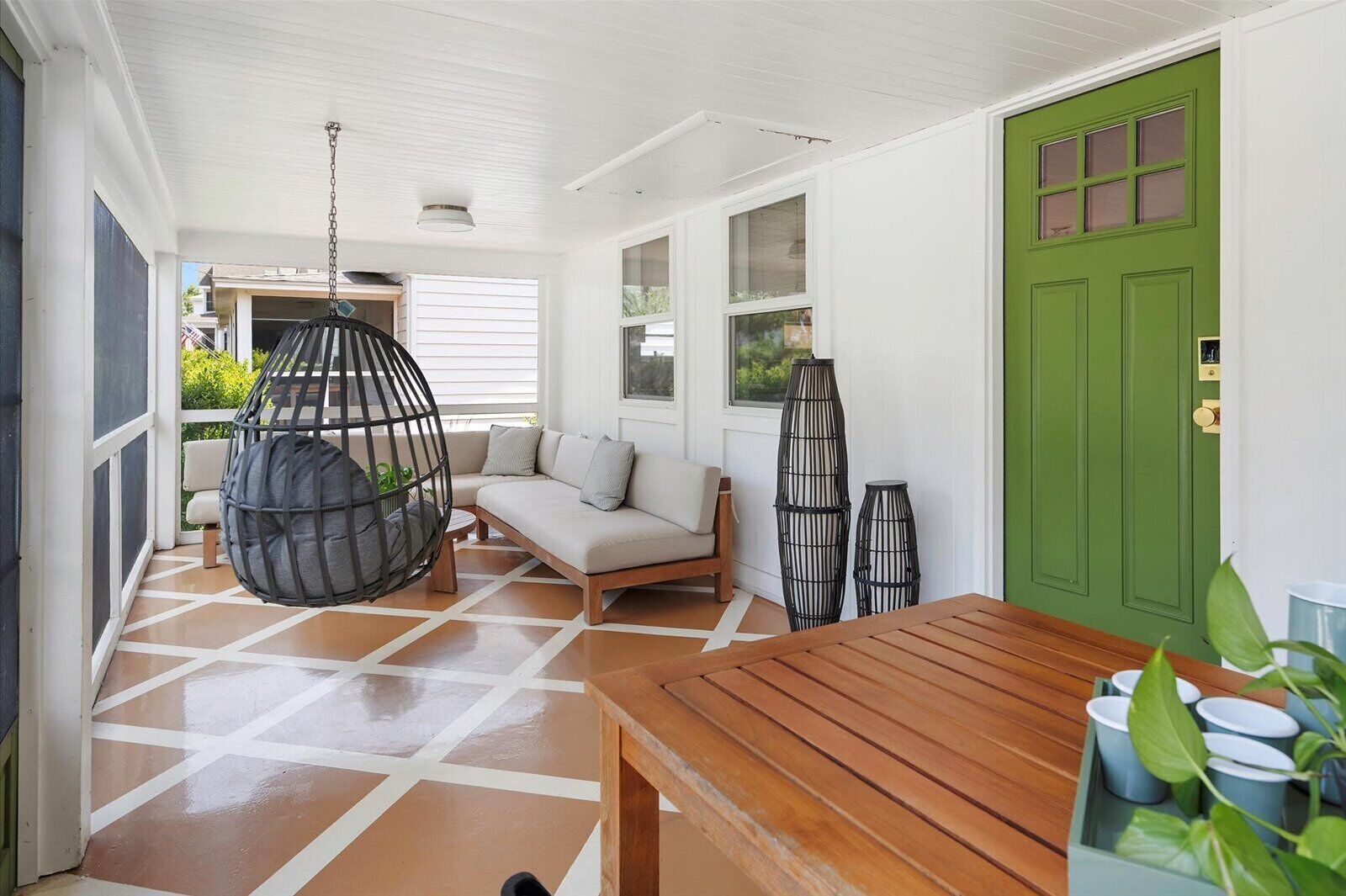 Un espacio interior acogedor con un banco de madera, una silla colgante y una puerta verde.