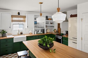 Uma cozinha com armários verdes, bancada de madeira, pia, fogão e luminárias pendentes.