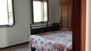 A bedroom with a bed, wooden wardrobe, and two windows.
