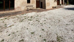 A two-story stone building with a gravel courtyard, wooden benches, and a clear blue sky.