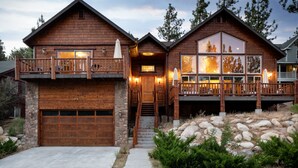 A two-story wooden house with a stone garage, a balcony, and a large window.