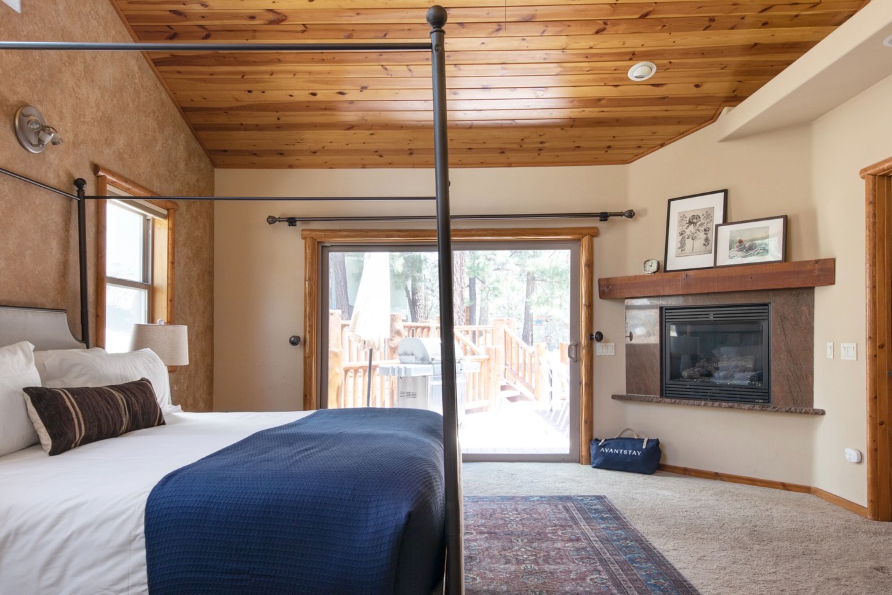 Een slaapkamer met een groot bed, houten plafond, open haard en uitzicht op een terras.