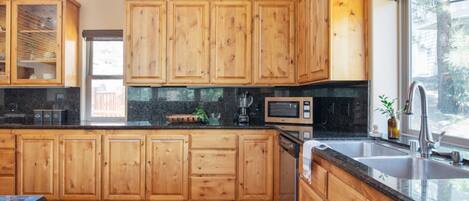 A modern kitchen with wooden cabinets, a granite countertop, a built-in microwave, and a large window providing natural light.