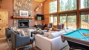 A cozy living room with a stone fireplace, comfortable seating, and a pool table.