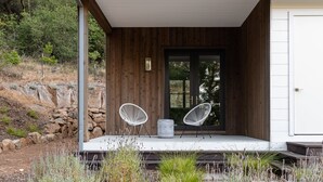 A wooden exterior with a covered porch, two white chairs, and a stone wall in the background. - Syrah by AvantStay | Hilltop Haven in Sonoma | Private Pool + Patio (Sonoma)