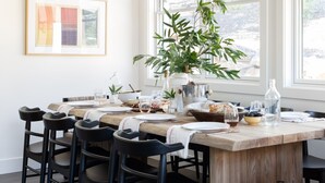 A dining area with a wooden table set for six, surrounded by black chairs. There is a large potted plant on the table, and a framed artwork on the wall. - Syrah by AvantStay | Hilltop Haven in Sonoma | Private Pool + Patio (Sonoma)