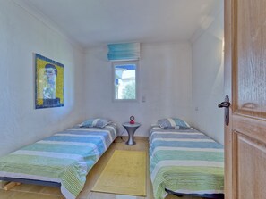 Een kleine, goed verlichte kamer met twee eenpersoonsbedden, een tafeltje, een raam met uitzicht en een deur.