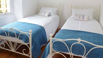 Two single beds with white frames and blue bedspreads in a room with wooden flooring and white walls.
