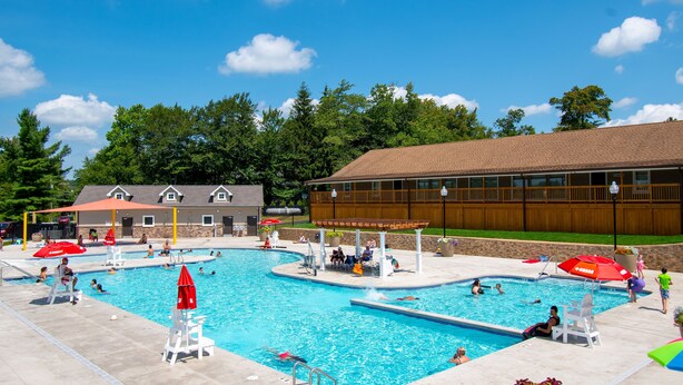 A large outdoor swimming pool with multiple lanes, surrounded by a wooden fence and a building with a sloped roof. - 6 Bedroom sleeps 17 in the Heart of Poconos near everything  (Tobyhanna)