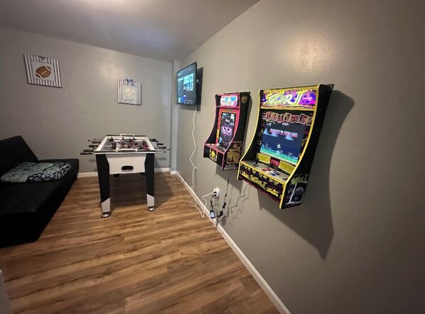 Una sala de estar con mesa de fútbol de mesa, dos juegos de arcade, un televisor y un sofá.