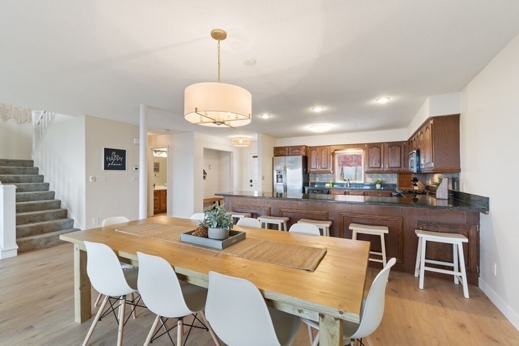A modern kitchen with dark wooden cabinets, a central island, and a dining area with a wooden table and white chairs.