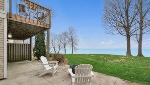 Une terrasse couverte avec deux fauteuils Adirondack, une terrasse en bois et une vue sur un lac.
