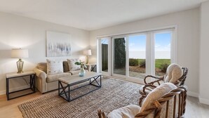 Un salon spacieux comprenant un canapé, une table basse et un fauteuil. Une grande fenêtre offre une vue sur l’extérieur.