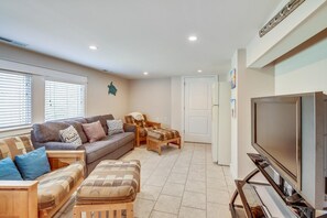 Una sala de estar con sofá, reposapiés y sillón, televisión y puerta que da a otra habitación.
