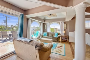 A spacious living room with a large window, a ceiling fan, and a view of the outdoors.