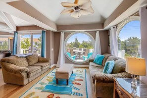 A spacious living room with a large round window, a ceiling fan, and a view of an outdoor patio.