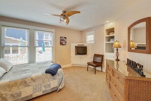 A bedroom with a bed, a television, a chair, a dresser, and a ceiling fan.