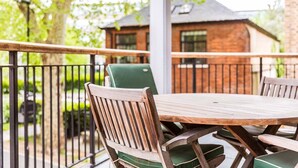 A wooden table and chairs on a balcony with a metal railing, overlooking a brick building. - Bright & Comfortable Angel Apartment (London)