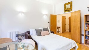 A bedroom with a bed, bedside tables, a chair, a small table, a radiator, and a bookshelf. - Bright & Comfortable Angel Apartment (London)