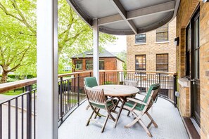 A covered outdoor patio with a round table and four chairs, surrounded by a metal railing. - Bright & Comfortable Angel Apartment (London)