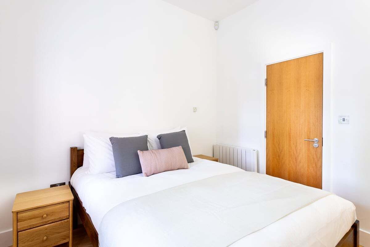 A bedroom with a single bed, a wooden nightstand, a wooden door, and a white radiator.