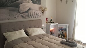 A bedroom with a large bed, a headboard with a painting, a minibar, and a window with curtains. - "FORTUNA" Luxury double room in prestigious Villa with shared pool. (Mazara del Vallo)