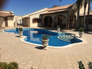 Ein Pool mit geschwungener Form, umgeben von einer gefliesten Terrasse und Kübelpflanzen.
