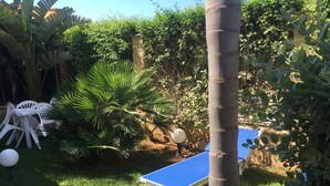 A garden with two ping pong tables, white plastic chairs, and a palm tree. - "FORTUNA" Luxury double room in prestigious Villa with shared pool. (Mazara del Vallo)