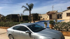 A silver sedan parked in a driveway with a swimming pool in the background. - "FORTUNA" Luxury double room in prestigious Villa with shared pool. (Mazara del Vallo)