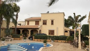 A two-story building with a tiled roof, a swimming pool, and palm trees. - "FORTUNA" Luxury double room in prestigious Villa with shared pool. (Mazara del Vallo)
