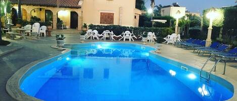 Una piscina rodeada de sillas de descanso y un edificio con techo de tejas.