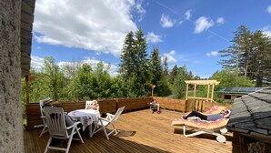 Una terraza de madera con mesa y sillas, un área de estar cubierta y una pérgola.