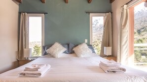 A neatly made bed with white linens and fluffy pillows, a bedside table with a lamp, and a window with curtains. - VC2 - LUXURY 2 BEDROOM APARTMENT CERRO CATEDRAL (San Carlos de Bariloche)
