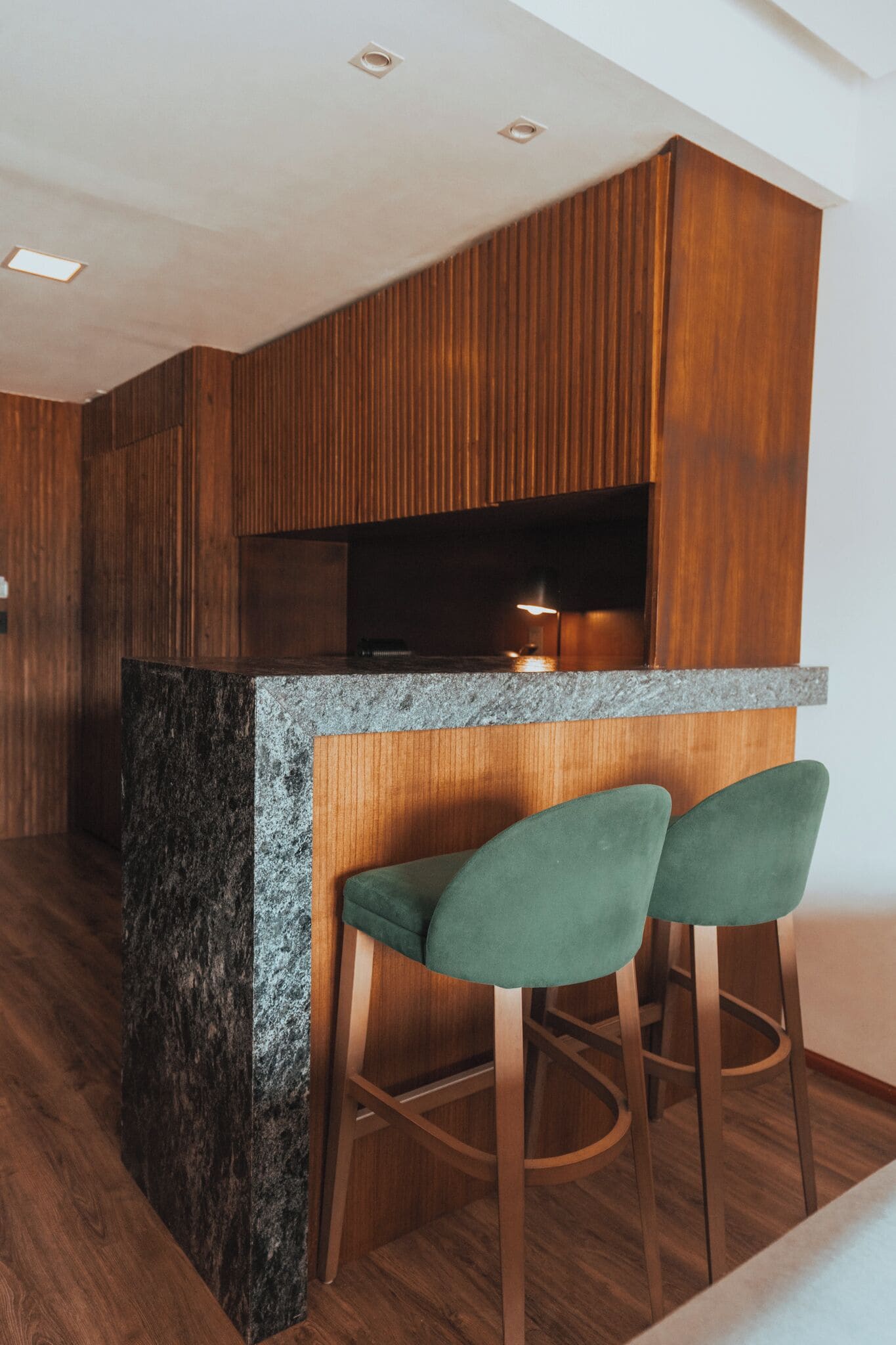 A modern kitchen with wooden cabinets, a granite countertop, and two green bar stools.